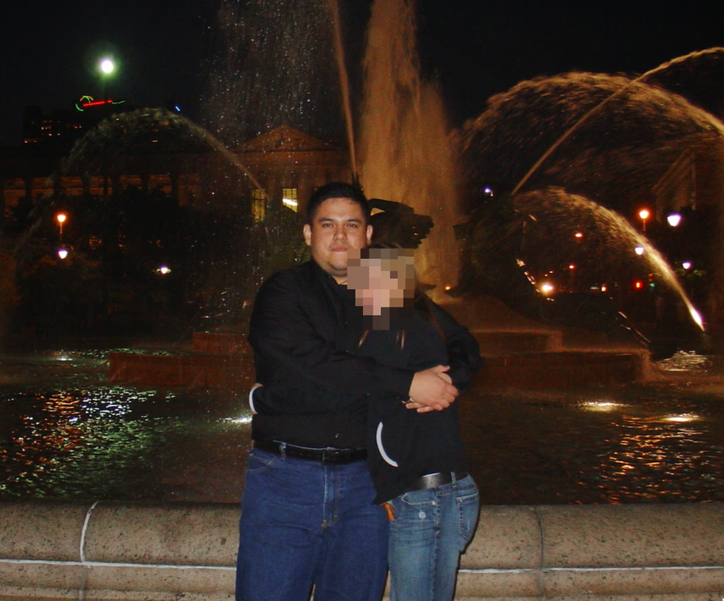 A man and a woman are hugging in front of a fountain at night.