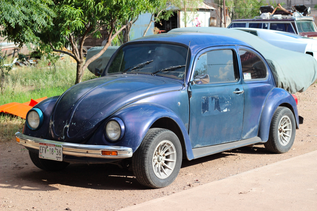 A dark blue (almost deep purple) Volkswagen Beetle car with tinted windows and rough spots on the paint.